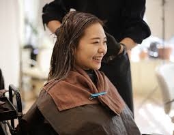 A woman sitting in a salon chair, having her hair trimmed by a female hairstylist.